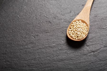 Raw white quinoa seeds in wooden spoon on black stone background. Concept of healthy and gluten free food.の写真素材