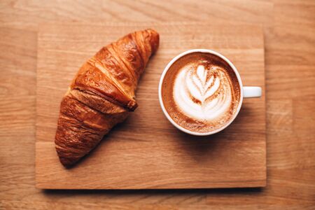 Cappuccino with beautiful latte art and croissant on wooden background on the table. Perfect breacfast in the morning. Rustic style.の写真素材
