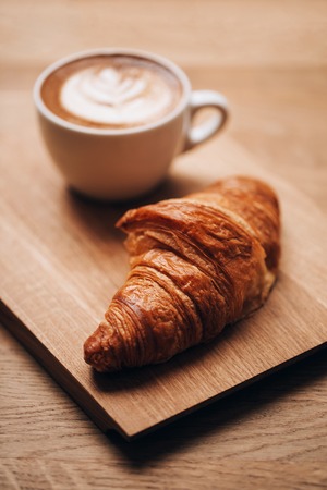 Cappuccino with beautiful latte art and croissant on wooden background on the table. Perfect breacfast in the morning. Rustic style.の写真素材