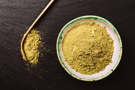 Spoon for matcha tea and green pouder in special ceramics sauser. Black background. Photo made in flat lay style. Focus is on matcha pouder.の写真素材