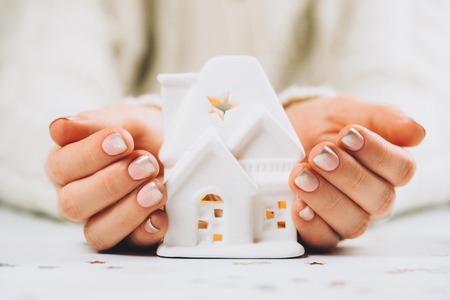 Female hands holding and saving small white house with a roof and lights.の写真素材