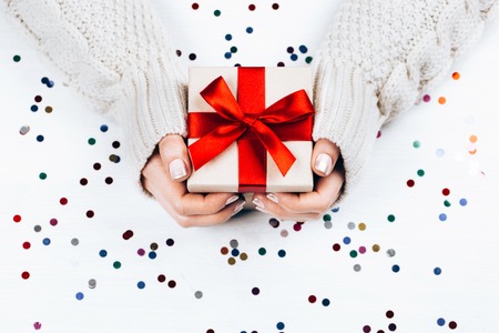 Female hands holding present with red bow on white rustic sparkling background. Festive backdrop for holidays: Birthday, Valentines day, Christmas, New Year. Flat lay styleの写真素材
