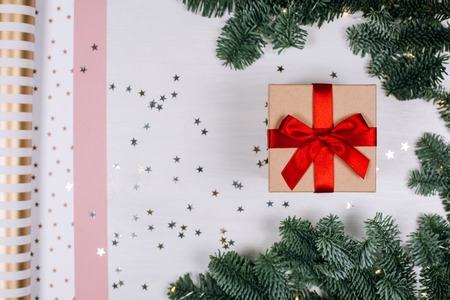 Christmas gift with red bow, fir branches, stars and paper for packaging. Flat lay style.