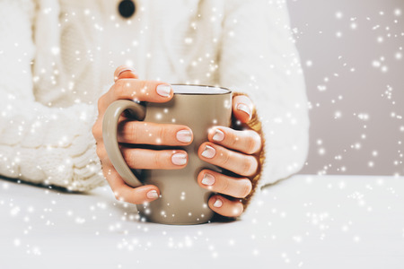 Woman with beautiful manicure holding cup of hot coffee. Falling snow. Winter conceptの写真素材