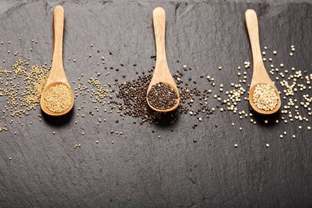 Quinoa, chia and amarantus seeds in wooden spoons on a black stone background. Super foods concept. Gluten free grains. Place for text. Lovely light gradient. Top view.の写真素材