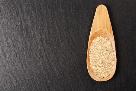 Raw white amaranth seeds in wooden spoon on black stone background. Concept of healthy and gluten free food.の写真素材