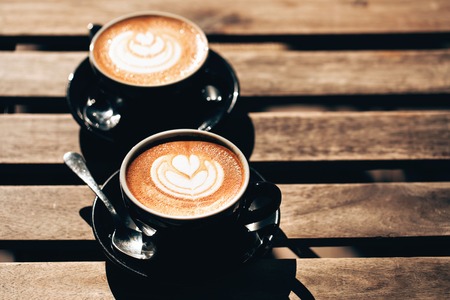 Two cups of cappuccino with latte art in black cups on wooden table. Morning coffee for couple in love. Top view.の写真素材