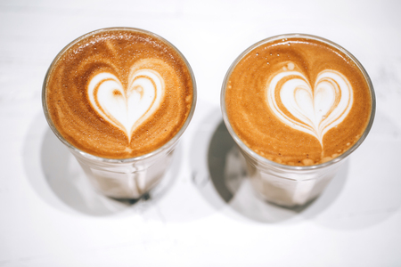 Two glass cups of cappuccino with latte art on white wooden table.の写真素材