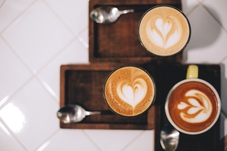 Tree cups of coffee with beautiful latte art and spoons on wooden boards, on white background.の写真素材