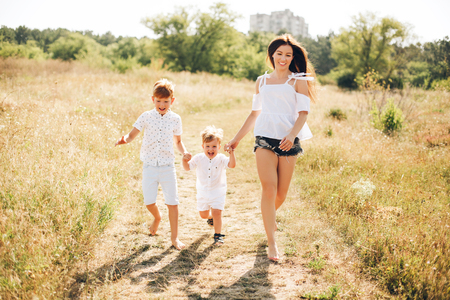 Mother with two sons running trough the field at sunny beautiful day. Boys are redheaded. 2 yers and 7 years old.の写真素材