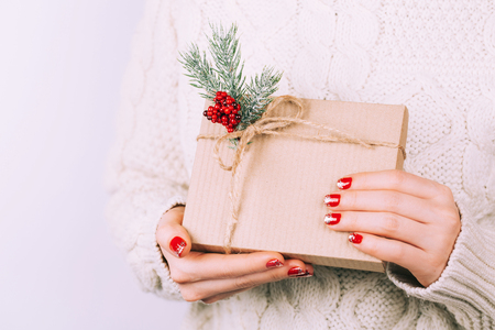 Womans hands with christmas gift box, decorated with pine branches. Accurate red festive manicure. There is place for text on the box.の写真素材