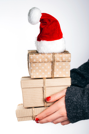 Woman in cozy sweater holding christmas craft gift boxes with santas hat. Chrismas coming concept.の写真素材