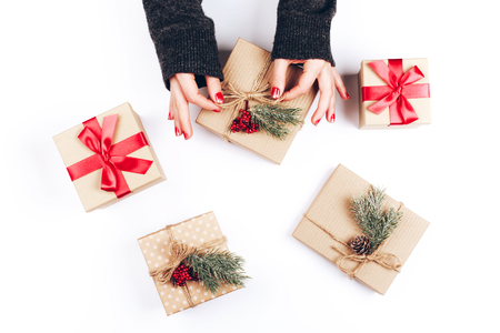 Womans hands and five vintage minimalistic Christmas gift boxes, decorated with pine cones, pine branches and red berriesの写真素材