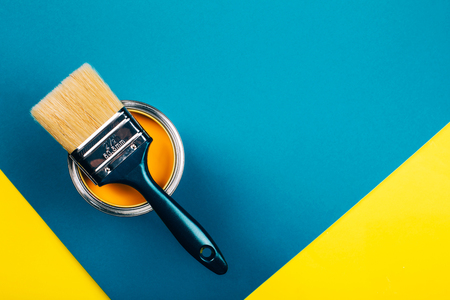 Brush on open can of yellow color paint on yellow and blue background. Flat lay style. Renovation concept.の写真素材