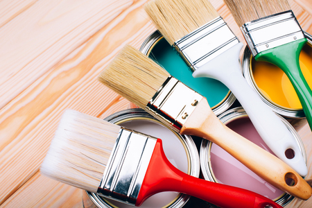 Four open cans of paint with brushes on them on wooden natural background. Yellow, white, pink, turquoise colors.の写真素材