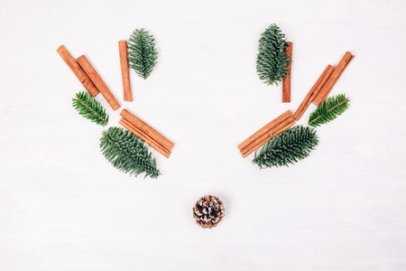 Deer face made of fir branches, cinnamon sticks and pine cone. White wooden rustic background. Winter flat lay style picture.の写真素材