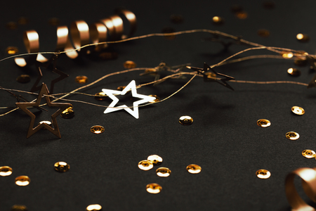 Golden decor of ribbons, confetti and star garland on black background. Selective focus. Festive concept.の写真素材