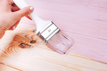 Womans hand with white brush applying pink paint on wooden furniture. Renovation concept.の写真素材