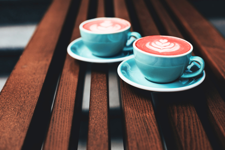 Two cups of Living Coral cappuccino on wooden background. Beautiful foam, greenery ceramic cups. Color of the year 2019の写真素材