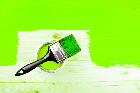 Brush with black handle on open can of ufo green paint on half painted wooden board. Renovation concept.の写真素材