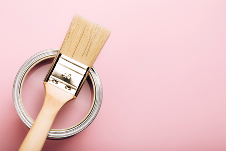 Brush with wooden handle on open can of pink paint on pastel background. Renovation concept. Macro.の写真素材
