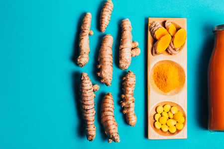 Turmeric in different conditions: fresh, dry root, pills, powder and cut plant on blue background. Flat lay style. Place for text.の写真素材
