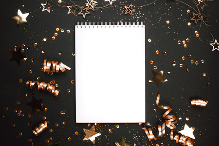 Holiday golden decorations and white notebook on black background. Flat lay style. Planning concept.の写真素材