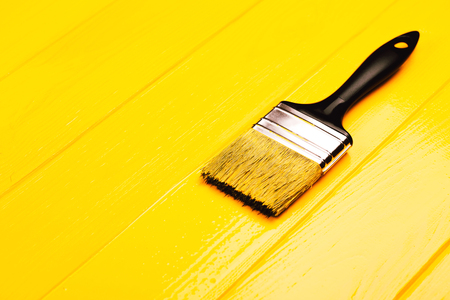 Paintbrush with black handle on yellow freshly painted wooden background. Repairing concept. Vertical photo.の写真素材