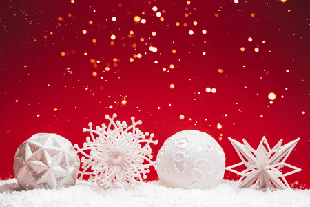 Four Christmas white decorative toys on red background with snow. Festive concept.の写真素材