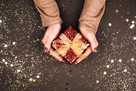 Sparkling red gift box with golden bow in womans hands. Winter concept.の写真素材