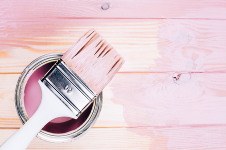 White brush on open can of pink color on painting wooden board. Renovation concept. Place for text.の写真素材