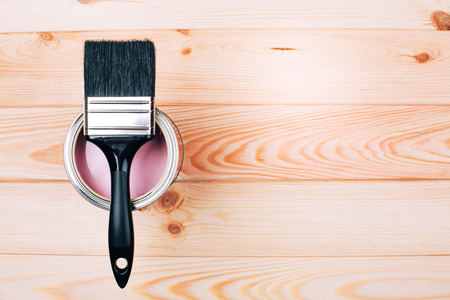 Brush with black handle on open can of pink color of paint on natural wooden board. Renovation concept.の写真素材