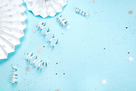 Holiday frame is made of silver and white decorations and sparkling confetti on blue pastel background. Festive concept. Place for text.の写真素材