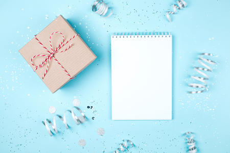 Craft gift box with blank white vertical notepad and silver tinsel on blue pastel background. Festive concept. Flat lay style.の写真素材