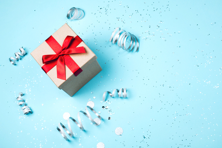 Craft gift box with red satin bow and sparkling silver tinsel on blue pastel background. Festive concept. Place for text.の写真素材