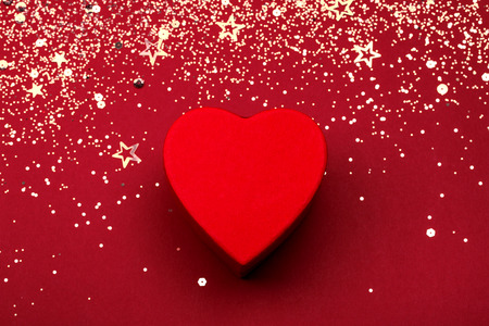 Heart shaped box with golden glitter and star confetti on red festive background. Valentines holiday concept. Top view.の写真素材