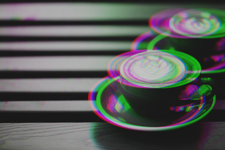 Two cups of cappuccino with glitch effect and latte art on wooden table.