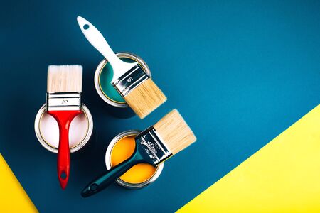Three open cans with brushes on them on yellow and blue background. Yellow, pink and turquoise...