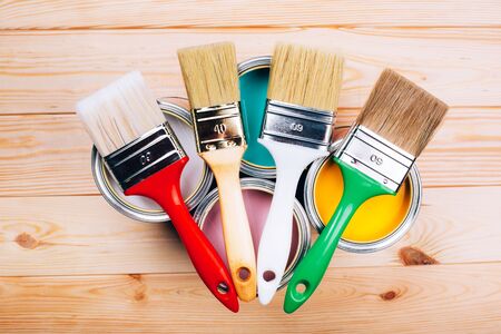 Four open cans of paint with brushes on them on wooden natural background. Yellow, white, pink, turquoise colors. Flat lay style.の写真素材