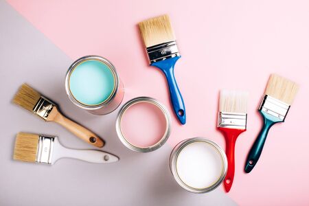 Three open cans of pastel paint with five brushes on pink and grey background. Renovation concept.の写真素材