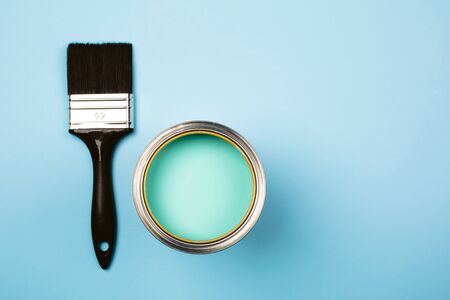 Brush with black handle on open can of teal paint on blue pastel background. Renovation concept. Macro.の写真素材
