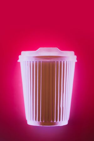 Close up of coffee to go cup in neon light on bright pink background. Eco concept. Place for text.の写真素材