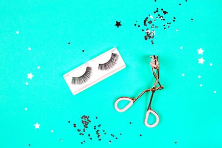 Eyelash curler and eyelashes on mint background with glitter. Flat lay style.