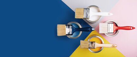 Banner with four open cans of paint with brushes on them on bright symmetry background. Yellow, white, pink, blue colors of paint. Top view.の写真素材