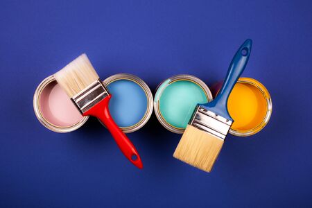 Four open cans of paint with brushes on blue background. Yellow, blue, pink, turquoise colors of...