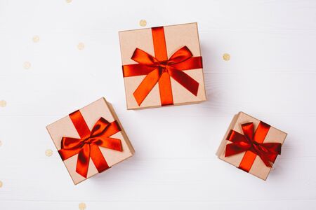 Three present boxes with red bow on white wooden background with golden confetti. Flat lay, place for text.の写真素材
