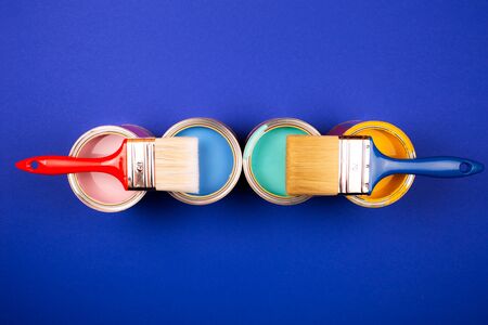 Four open cans of paint with brushes on blue background. Yellow, blue, pink, turquoise colors of paint. Top view.の写真素材
