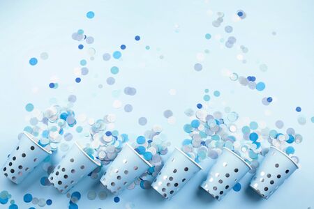 Beautiful festive cups in a row with colorful confetti on blue pastel background. Flat lay style. Place for text.の写真素材