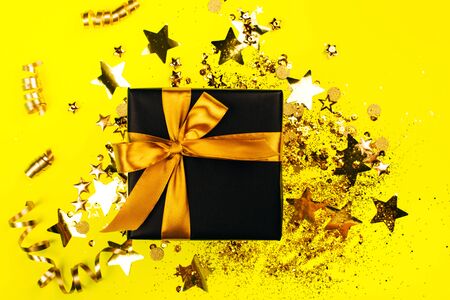 Black gift box with golden bow on yellow background with glitter. Holiday concept.の写真素材