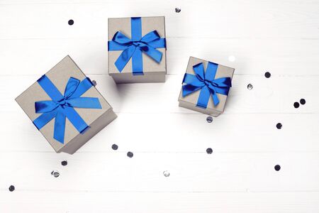 Three present boxes with blue bow on white wooden background with confetti. Flat lay, place for text.の写真素材